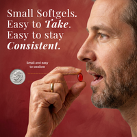 Man holding a small softgel pill next to a coin for size comparison on a red background.
